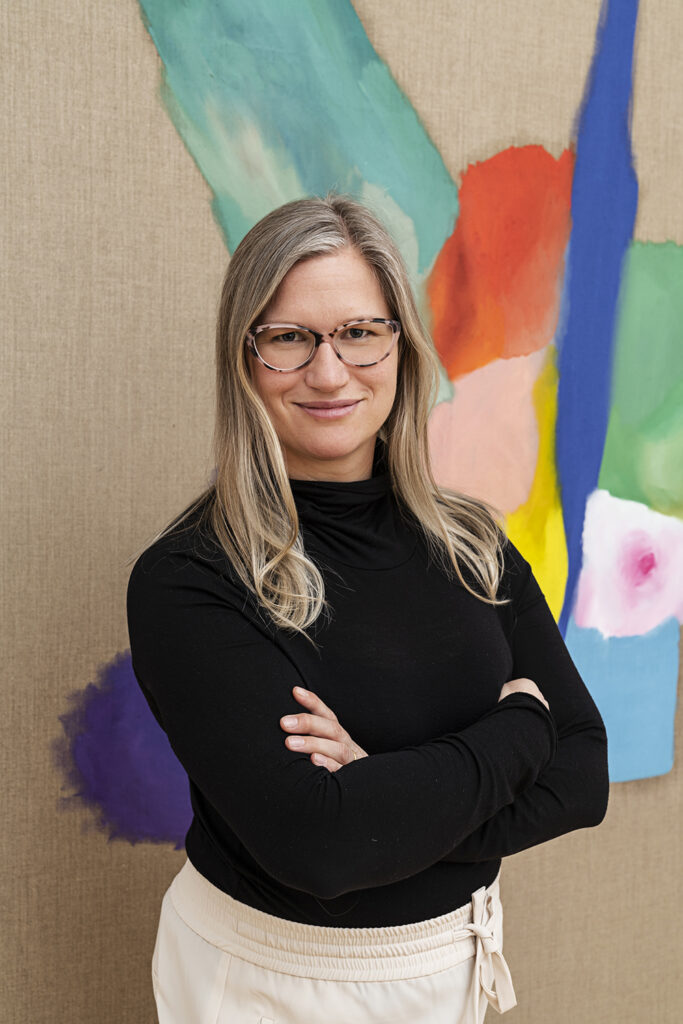 Portrait of the artist Lena Schmid-Tupou infront of one of her paintings